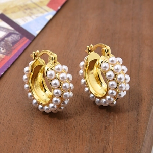 Macro view of gold-plated C-shaped earrings with white pearls on a wooden surface