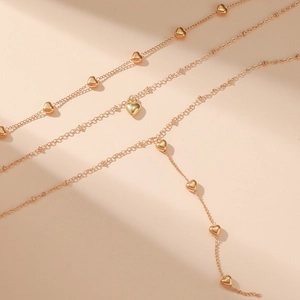 Detailed close-up of a multi-layer gold heart pendant necklace on a beige background