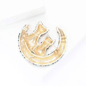 Detail view of gold moon and cats brooch with blue rhinestones and textured metal finish
