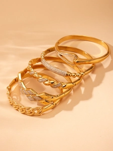 Dettaglio di cinque bracciali rigidi placcati oro con zirconi e diverse texture