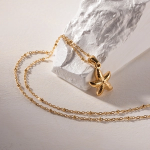 Detailed close-up of a gold starfish pendant necklace with beads on textured white rock