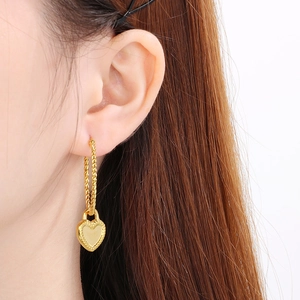 Gros plan d'une boucle d'oreille cœur doré avec créole torsadée et gravure fine