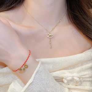 Close-up of gold plated horse pendant necklace and red woven bracelet on a model