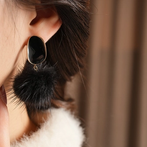 Close-up of black plush pom-pom earrings with elegant gold-rimmed oval studs