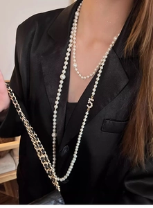 Detail of layered pearl necklace featuring a zircon number 5 pendant on black blazer