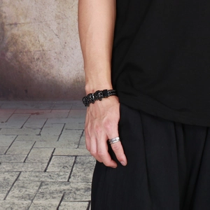 Close-up of a black skull bracelet and silver braided ring on a model hand