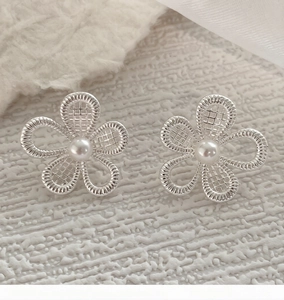 Macro shot of silver hollow flower stud earrings with elegant pearls on textured fabric