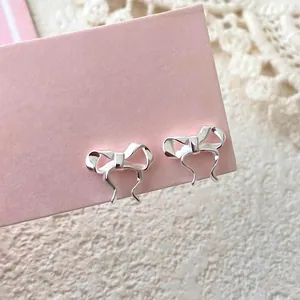 Polished S999 silver bow stud earrings presented on a pink card with lace background