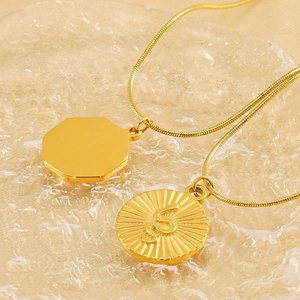 Gold snake relief pendant and octagonal coin necklaces on glass background