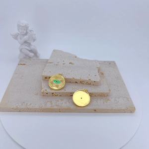 Detailed shot of a gold-plated evil eye pendant and smooth disc on beige stone plates