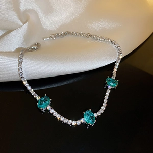 Detailed close-up of a silver four-leaf clover bracelet with green oval zircons on silk