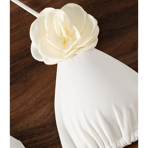 Chic white bikini top featuring a large 3D fabric rose on a dark wood background