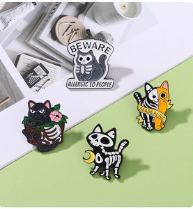 Set of four skeleton cat enamel pins with Beware Allergic to People text on a desk