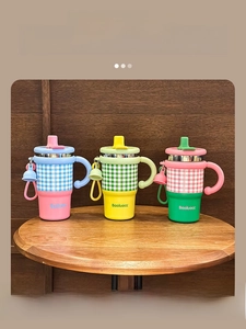 Three stylish plaid insulated coffee mugs with handles and straws on a wooden table