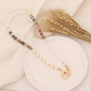 Close-up of Bohemian clay bead necklace with pearls and golden heart clasp on white linen