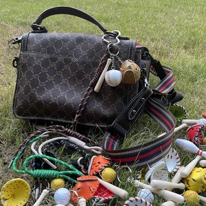 Detail of mini baseball bat and glove keychain charm on a brown patterned handbag