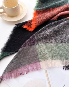 Detailed close-up of cashmere-feel colorful plaid scarf with soft fringe on a desk