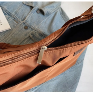 Detail view of the brown nylon tote bag with silver zipper closure and leather logo patch