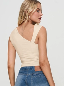 Détail du haut en tricot beige à une épaule et du jean avec patch en cuir gaufré