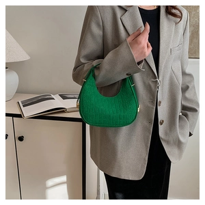 Close-up of a green crocodile embossed PU leather handbag held by a model in a gray suit