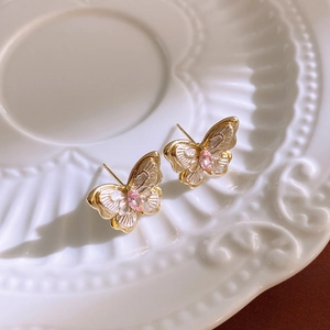 Detailed view of butterfly stud earrings with pink zircon on a vintage white ceramic plate