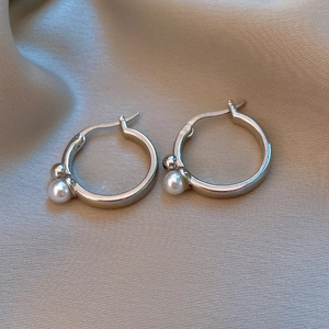 Gros plan détaillé des boucles d'oreilles perles sur soie, soulignant le fini argenté
