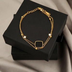 Detail of a gold double-layer titanium bracelet with a black square gem and zircon accents