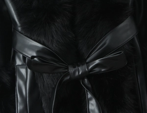 Detail of black faux leather coat featuring plush fur trim and an elegant bow tie design