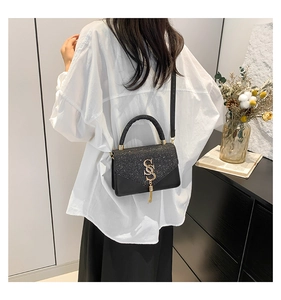 Detail view of black glitter shoulder bag with gold S-buckle and tassel on a model