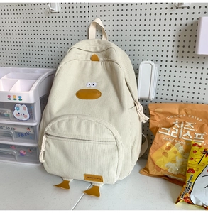 Detail of cute duck corduroy backpack in off-white with yellow accents on pegboard