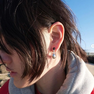 Detail of silver drop earrings with black bead on model against outdoor sky background