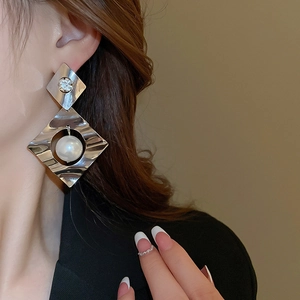 Detail of silver oversized geometric diamond stud earrings with a large pearl drop
