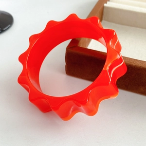 Macro view of bright orange wavy gear resin bangle with a polished high-gloss finish