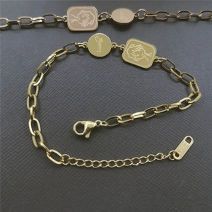 Detail of gold stainless steel bracelet with lucky tag and angel girl charm on grey surface
