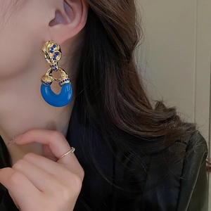 Close-up of elegant blue C-shaped drop earrings with gold inlay on a female model