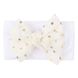 Soft white nylon baby headband featuring a large bow with shimmering gold polka dots