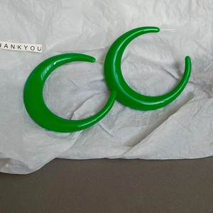 Close-up of glossy green crescent hoop earrings with silver pins on a minimal background