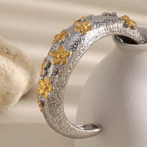 Macro shot of silver hammered cuff bracelet featuring gold flower accent on ceramic decor
