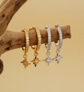 Macro shot of gold and silver S925 sterling silver star drop earrings on a wood branch