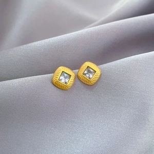 Macro detail of square zircon stud earrings with radiant gold texture on grey silk
