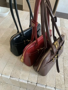 Three glossy leather bowling bags in black, red, and brown on stone steps