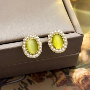 Detailed close-up of oval gold earrings with green cat-eye stone and pearl border