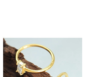 Detailed macro view of a gold-finish ring with a rectangle clear gemstone in 4-prong setting