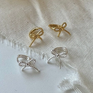 Elegant 925 sterling silver bow knot earrings in gold and silver finish on linen fabric