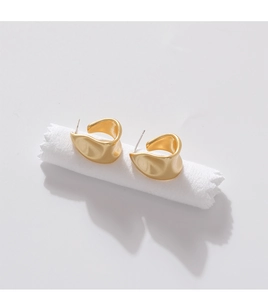 Macro detail of golden matte earrings with irregular wave design on white pedestal