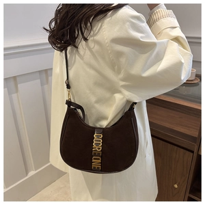 Detail of a brown suede crescent bag with gold COCRE ONE lettering on a model