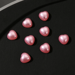 Close-up of eight pearlescent pink heart-shaped charms for nail art and jewelry
