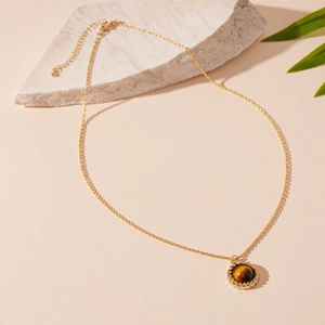 Vintage gold necklace with round brown tiger eye stone pendant on stone background