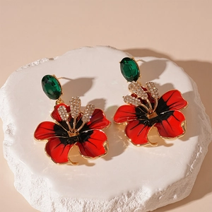 Détail macro de boucles d'oreilles fleur en émail rouge avec gemme verte et cristaux