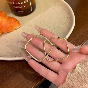 Close-up of large gold square hoop earrings held by hand in a warm lifestyle setting
